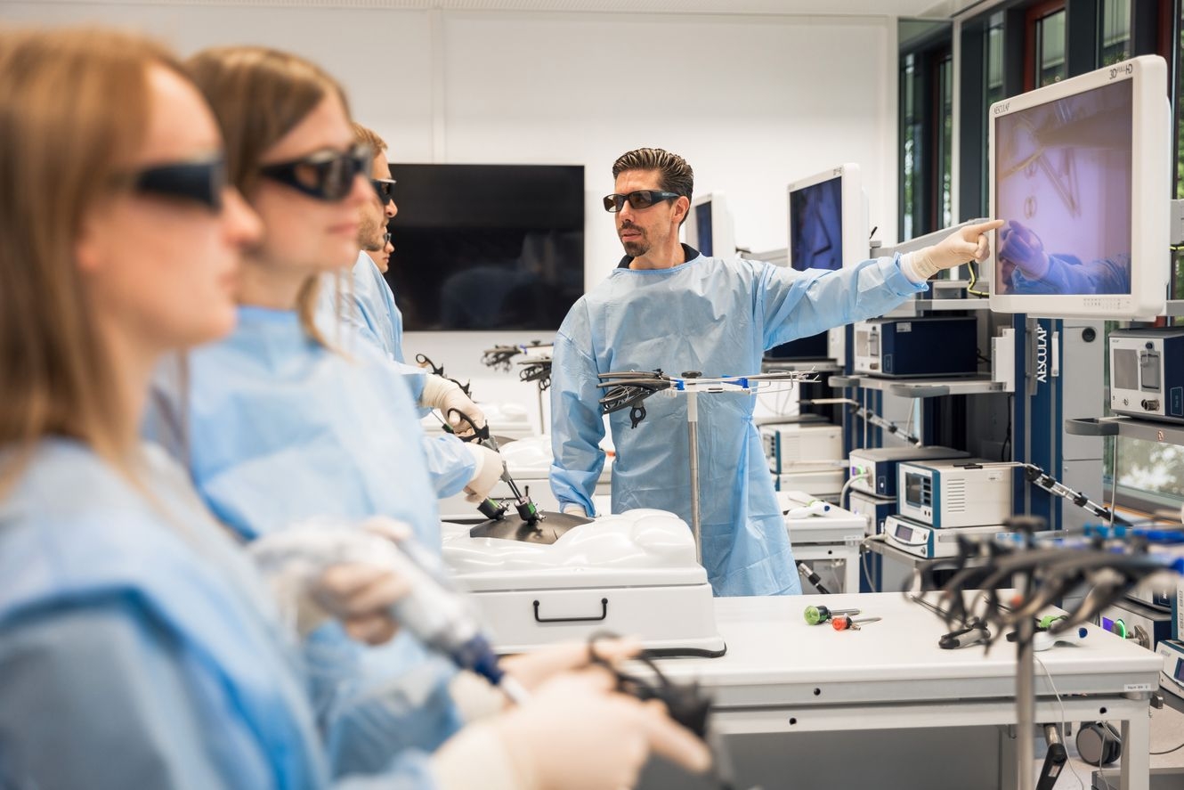 Medical training session with participants in blue gowns using surgical instruments and monitors in a high-tech lab Setting