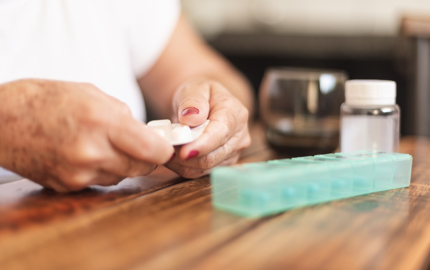 Uma mulher segura um frasco de comprimidos numa mão e um copo de água na outra, preparando-se para tomar medicamentos.