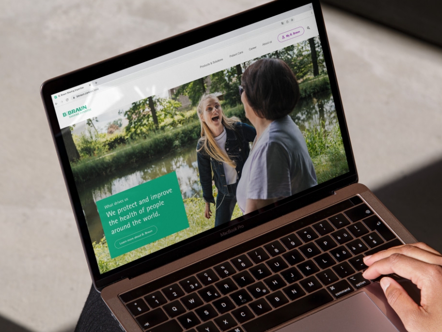 Um computador portátil com o site da B. Braun aberto e uma mão apoiada no canto inferior direito do computador portátil. 