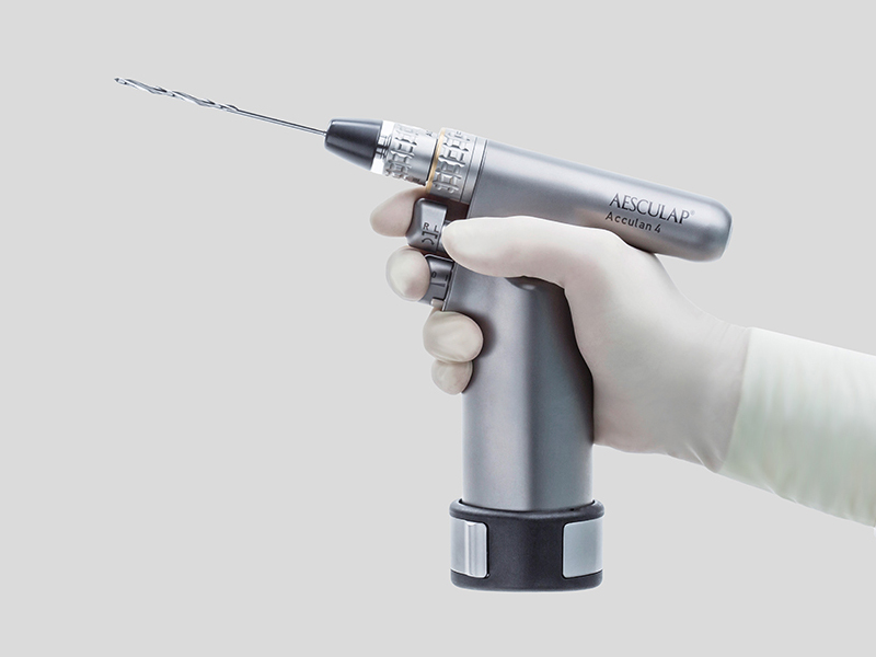 Uma mão com luva segura um motor cirúrgico elétrico