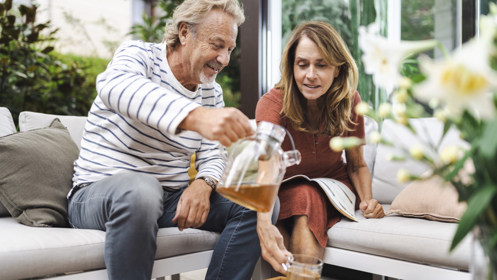 Um homem e uma mulher de meia idade sentados juntos no sofá e o homem serve uma chávena de chá à mulher
