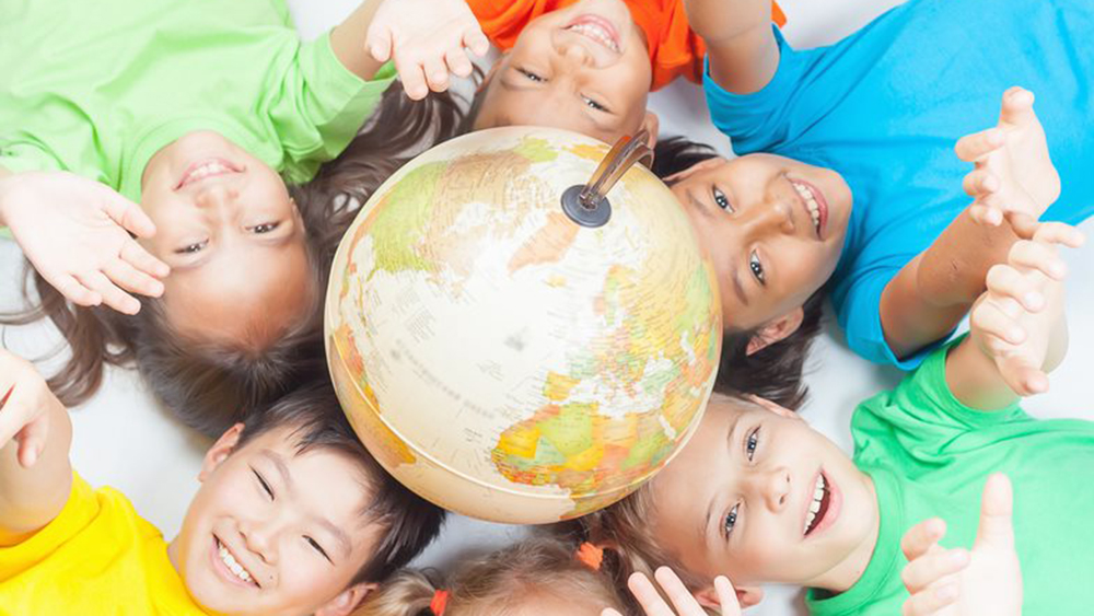 Crianças sorridentes deitadas à volta de um globo no chão, esticando os braços para cima.